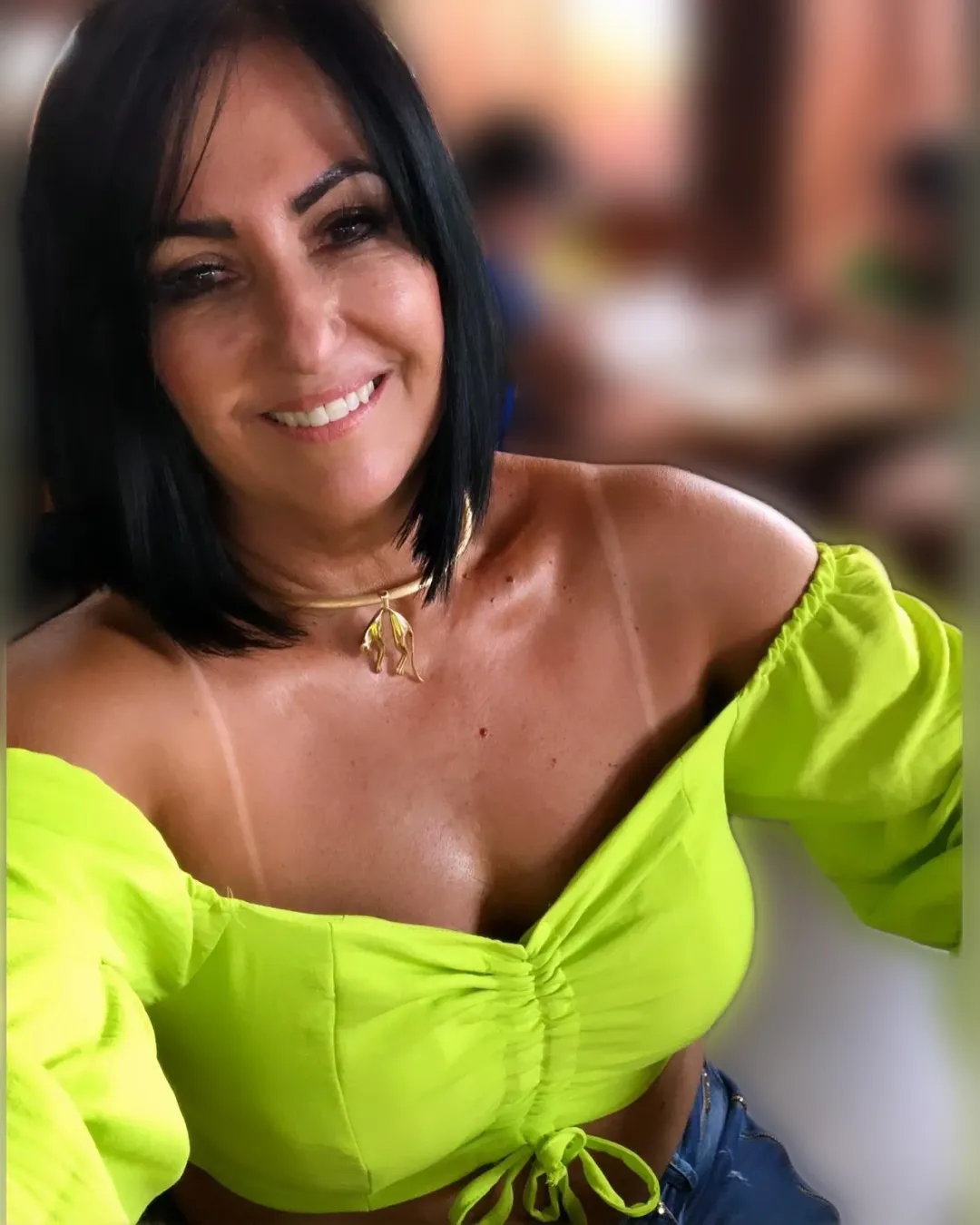 Cliente sorrindo em uma selfie, de blusa verde-limão, com a marquinha do biquíni nos ombros.