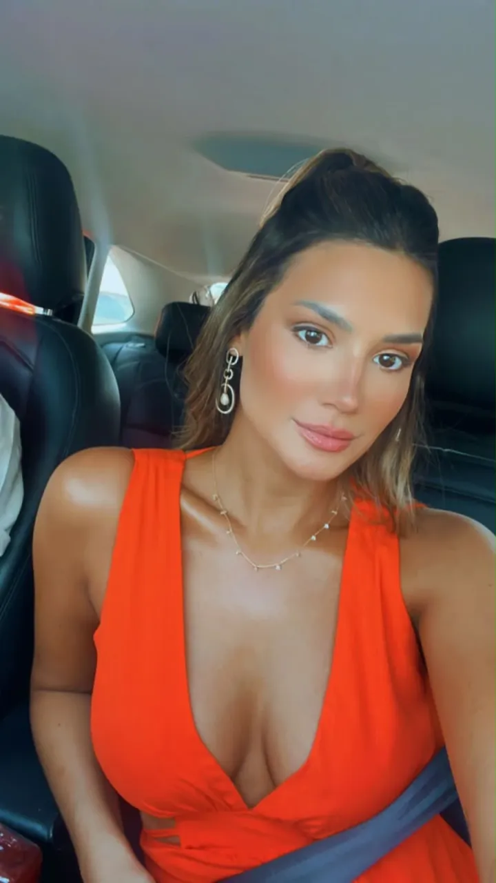 Cliente de vestido laranja em uma selfie no carro, com a pele bronzeada.