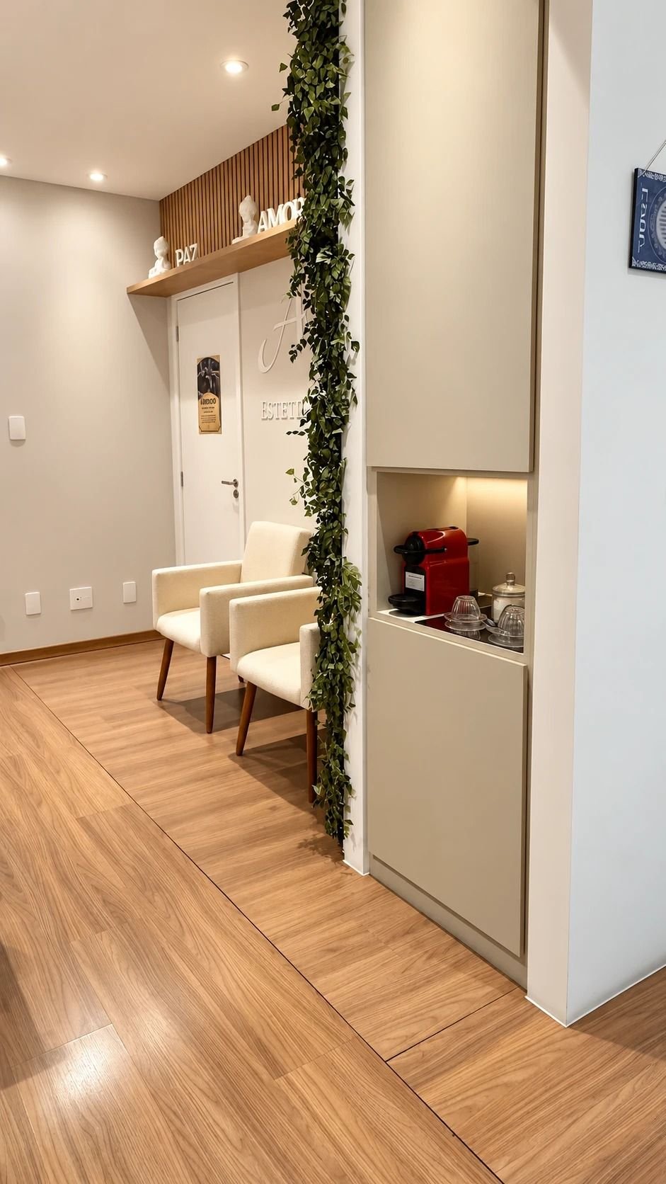 Recepção com poltronas, folhagem pendente e nicho iluminado com cafeteira e xícaras.